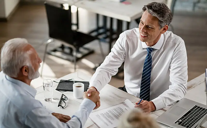 Dos personas dándose la mano después de un acuerdo con la mesa llena de papeles