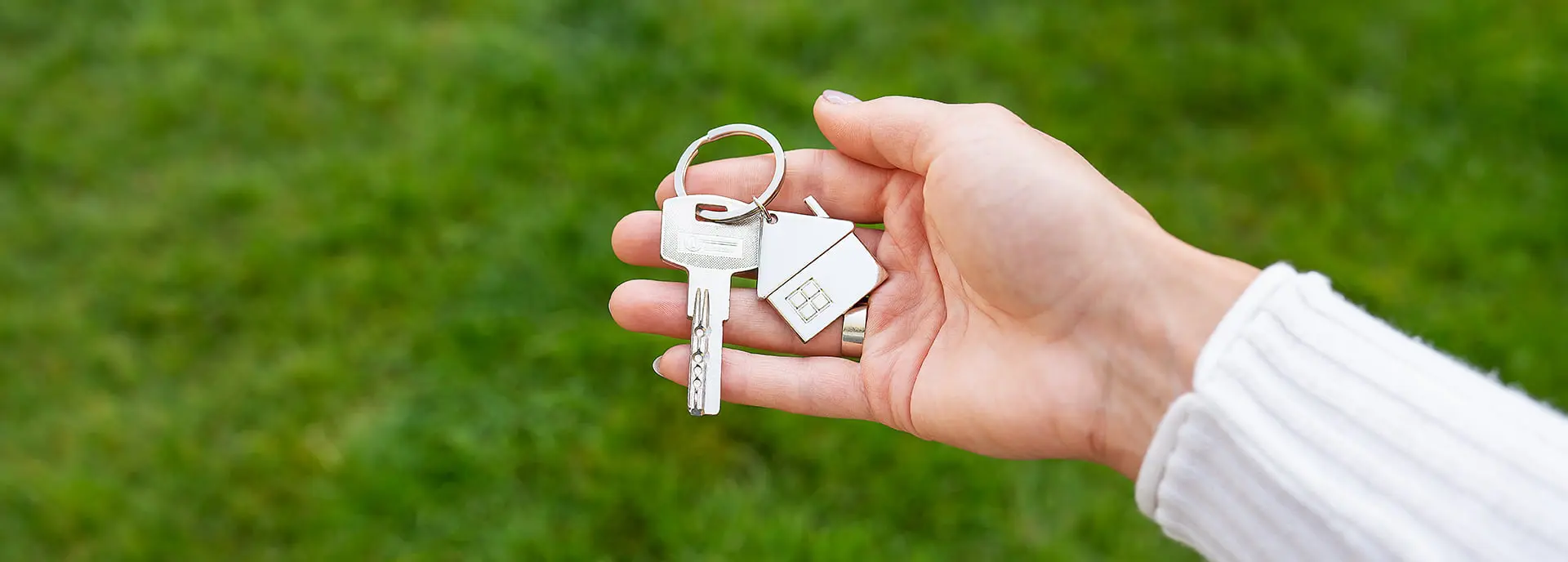 Primer plano de una mano sujetando una llave con un llavero de una casa